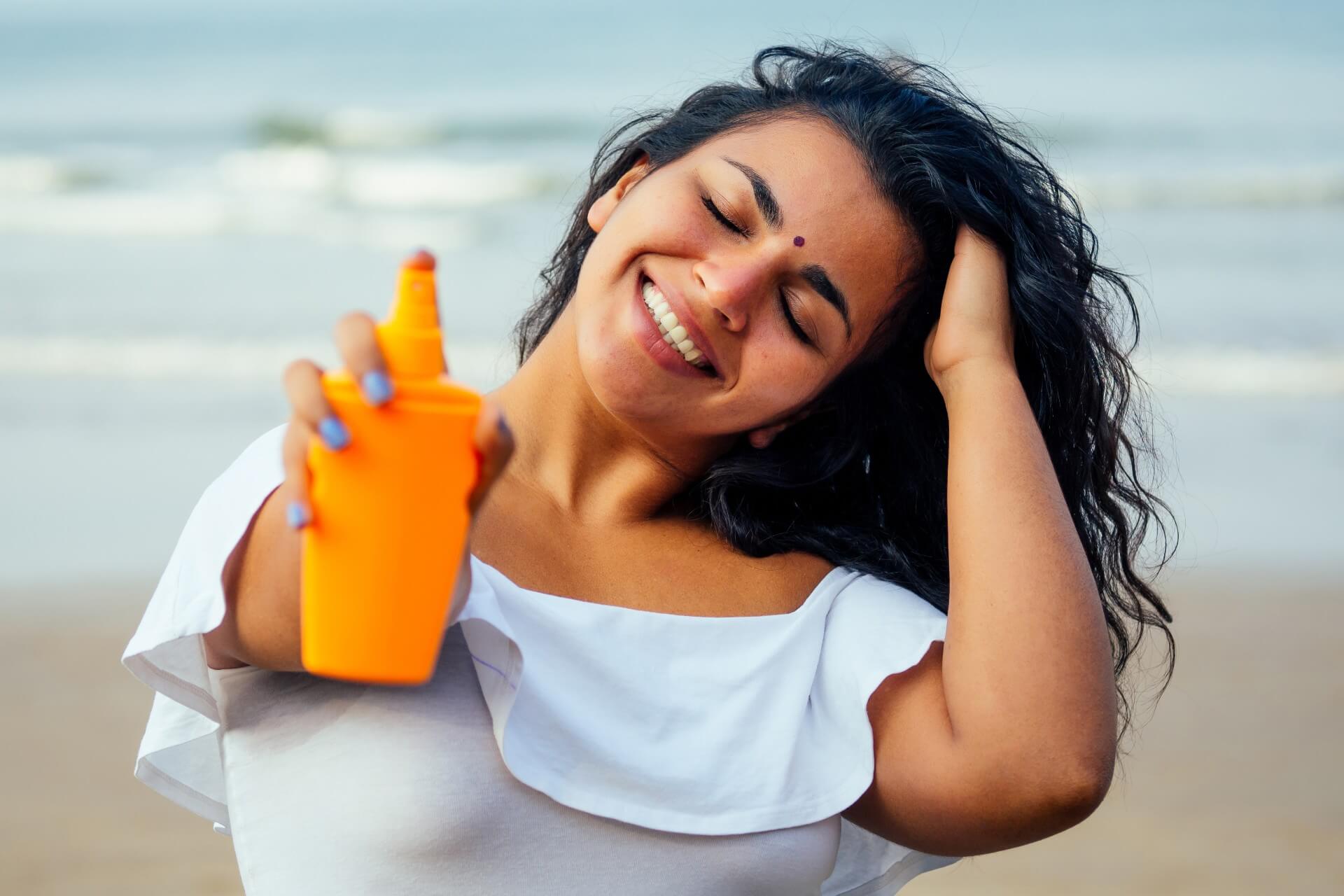 mulher na praia aplicando protetor solar para cabelos